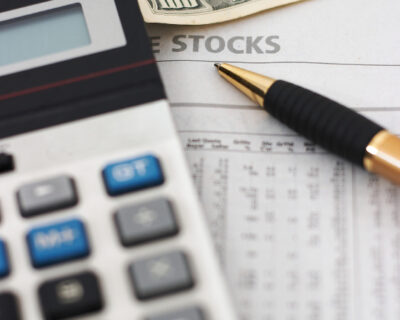 Stock market table analysis, calculator and pen indicates research and analysis, with cash, vertical orientation, shallow depth of field